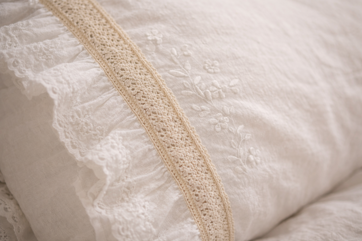 Détail de la broderie et de la dentelle sur une housse de coussin en coton, texture douce et finitions délicates.