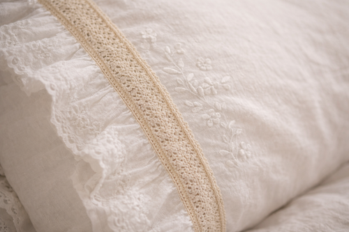 Détail de la broderie et de la dentelle sur une housse de coussin en coton, texture douce et finitions délicates.